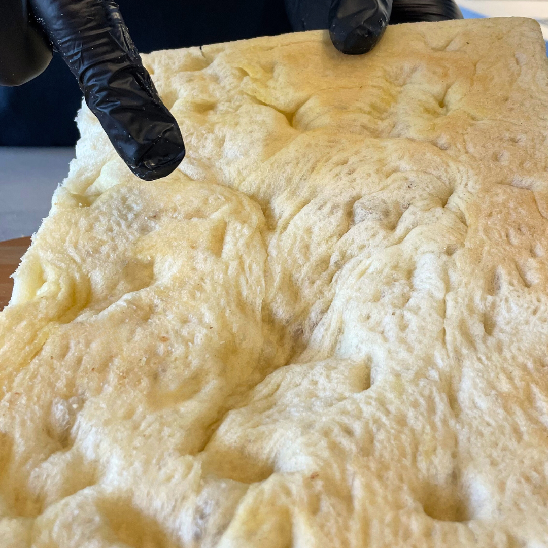 Foto prodotto Base Pizza Fermentata Classica da Agricoltura Biologica. Si vede una mano che sta indicando il retro della base pizza fermentata per mostrare da che lato va versato il pomodoro.