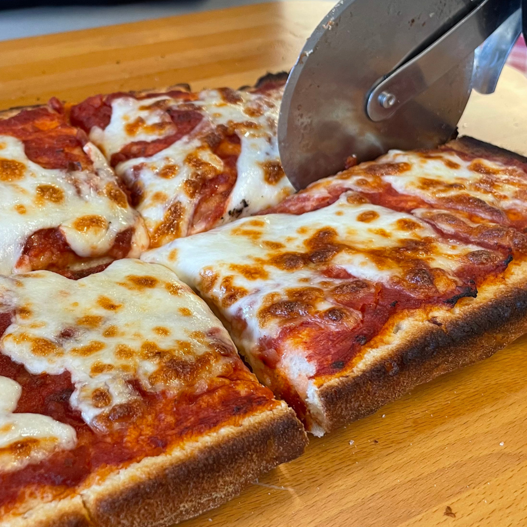 Foto prodotto Base Pizza Fermentata Classica da Agricoltura Biologica. Si vede la base pizza in versione margherita mentre viene tagliata da una rotella per pizza.