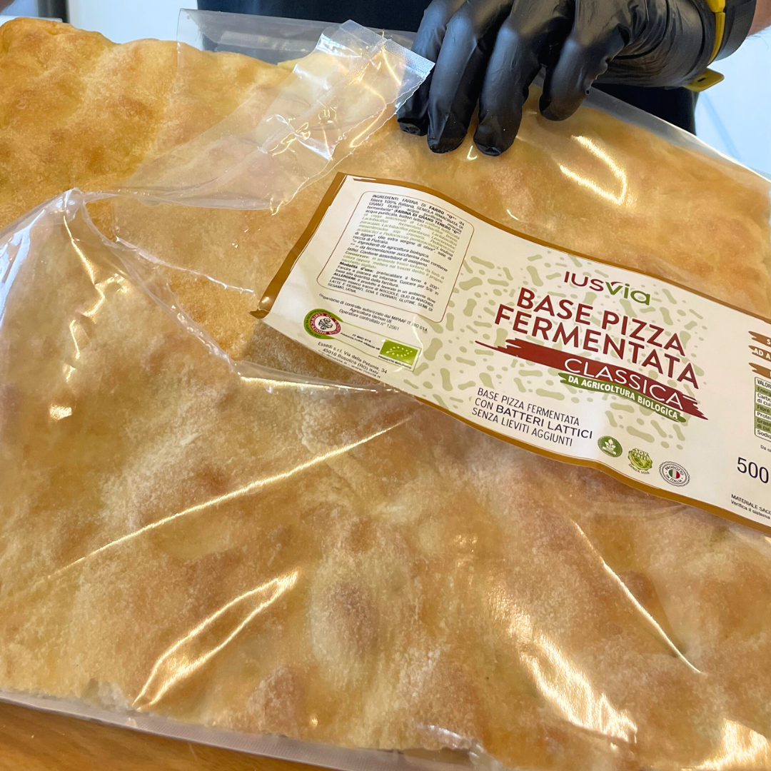Foto prodotto Base Pizza Fermentata Classica da Agricoltura Biologica. Si vede la base pizza mentre viene estratta dall'involucro pronta per essere farcita.