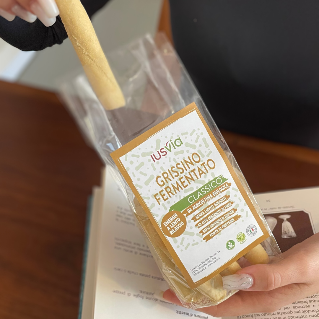 Foto prodotto Grissino Fermentato Classico da Agricoltura Biologica, un'alternativa alla barretta energetica. Si vede una persona che sta prendendo un grissino dal sacchetto mentre svolge mansione in ufficio.