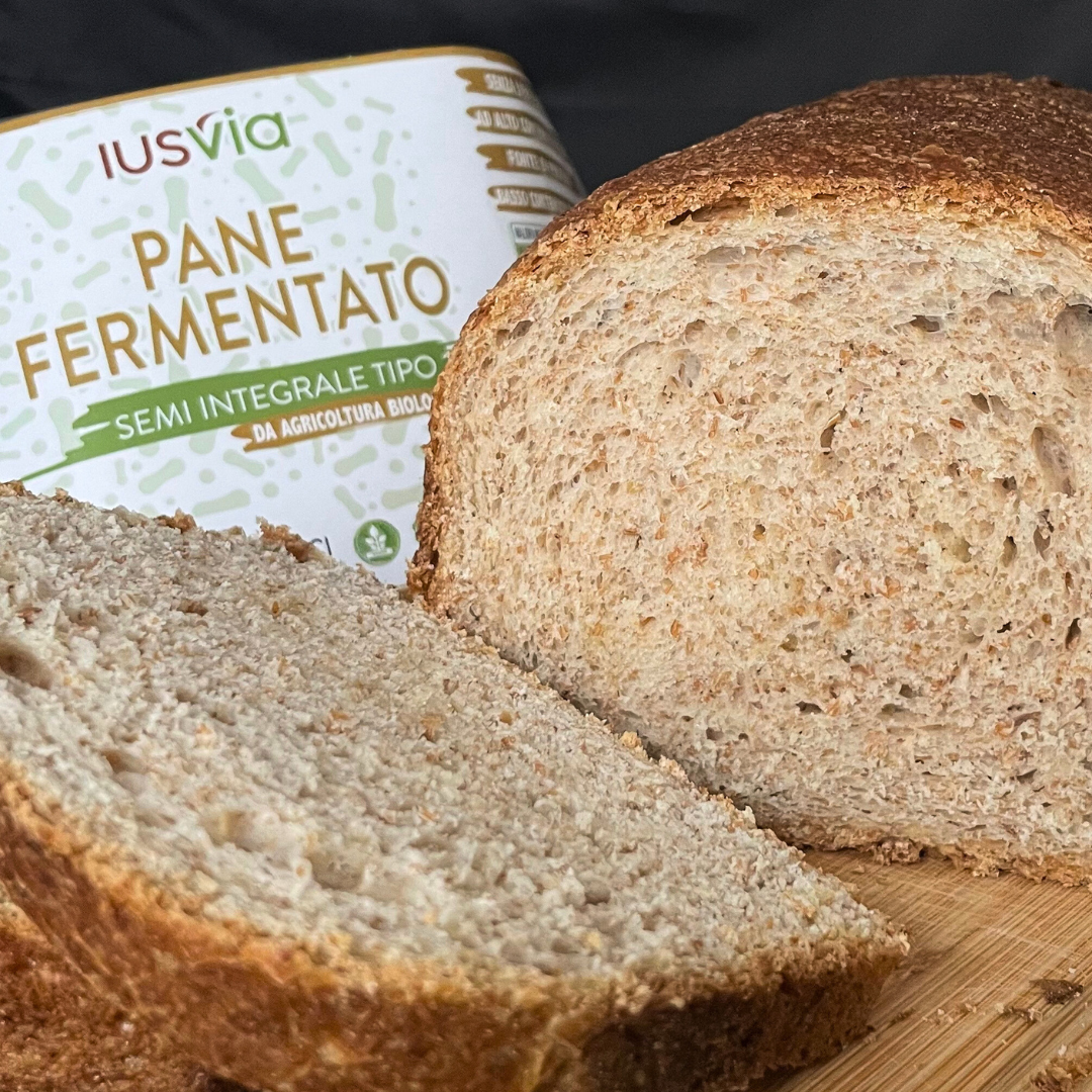 Foto prodotto Pane Fermentato Semi Integrale Tipo 2 da Agricoltura Biologica. Si vede una fetta di pane integrale che viene tagliata su un tagliere di legno. Nello sfondo c'è l'etichetta del prodotto.