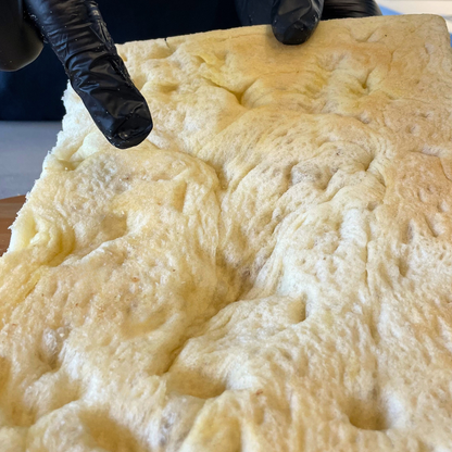 Foto prodotto Base Pizza Fermentata Classica da Agricoltura Biologica. Si vede una mano che sta indicando il retro della base pizza fermentata per mostrare da che lato va versato il pomodoro.