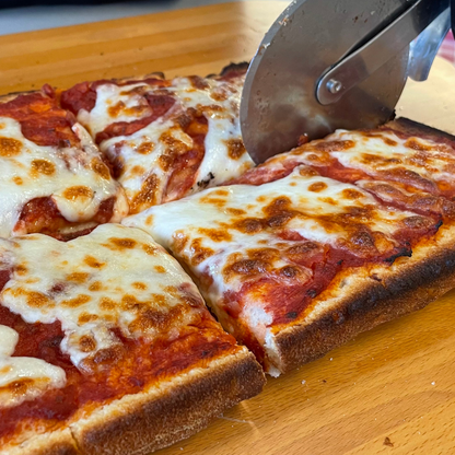 Foto prodotto Base Pizza Fermentata Classica da Agricoltura Biologica. Si vede la base pizza in versione margherita mentre viene tagliata da una rotella per pizza.
