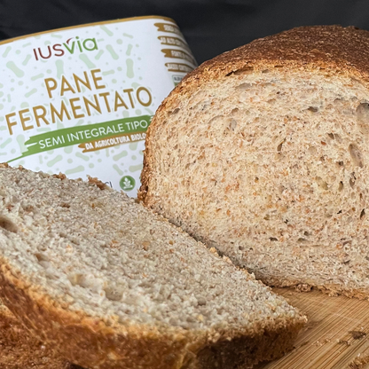 Foto prodotto Pane Fermentato Semi Integrale Tipo 2 da Agricoltura Biologica. Si vede una fetta di pane integrale che viene tagliata su un tagliere di legno. Nello sfondo c'è l'etichetta del prodotto.